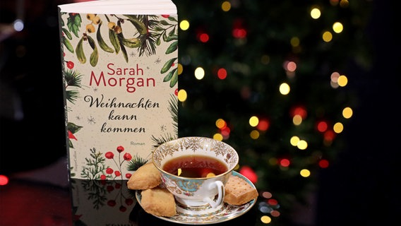Eine Tasse Tee neben einem aufgestellten Buch und einem Weihnachtsbaum - eat.READ.sleep.Folge © NDR Foto: Thorsten Schmidt