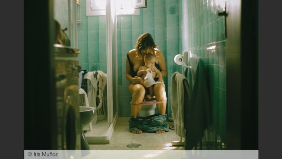 Eine Frau sitzt auf der Toilette und hat ein Baby auf dem Schoß; Bild von Iris Muñoz aus: "Eye Mama", teNeues Verlag © Iris Muñoz 