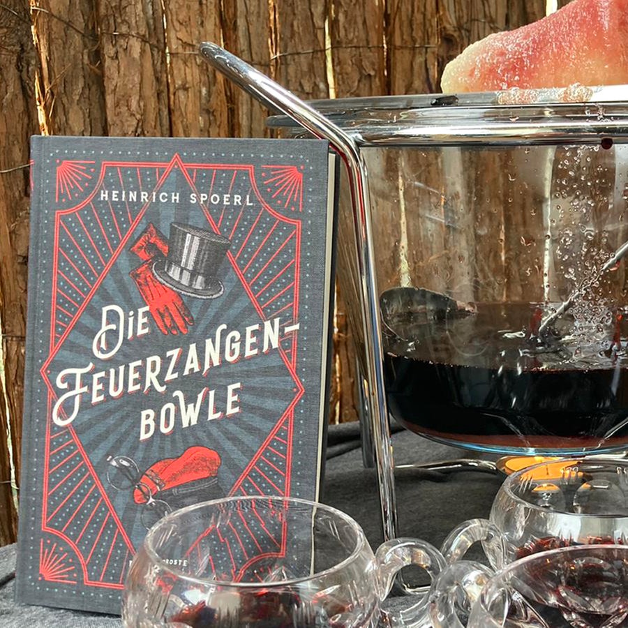 Das Buch von Heinrich Spoerl "Die Feuerzangenbowle" steht auf einem Tisch neben einer Feuerzangenbowle im Freien © NDR 