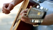 Zwei Hände spielen auf einer Gitarre. © Fotolia.com Foto: Georg Tschannett