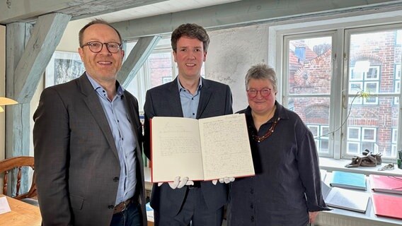 Zwei Männer und eine Frau lächeln in die Kamera und halten ein aufgeschlagenes Buch hoch. Zwei Männer und eine Frau lächeln in die Kamera und halten ein aufgeschlagenes Buch hoch. © NDR.de/ Hauke Bülow Foto: Hauke Bülow