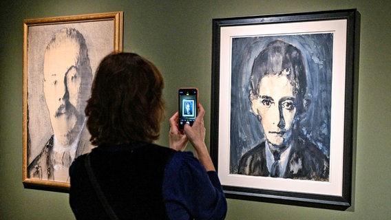 Una mujer utiliza su teléfono inteligente para fotografiar un cuadro de Franz Kafka, de Siegfried Herz, en una exposición en Praga © foto Alliance / CTK Foto: CTK Foto / Vit Simanek, Pinturas de Siegfried Herz