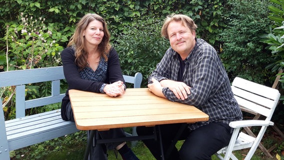 Das Schrifstellerpaar Mareike Krügel und Jan Christophersen sitzt an einem Tisch im Garten. © NDR Foto: Katja Weise