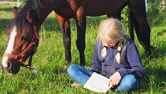 Ein Mädchen sitzt vor einem Pferd und liest ein Buch © NDR/Katharina Mahrenholtz Foto: Katharina Mahrenholtz