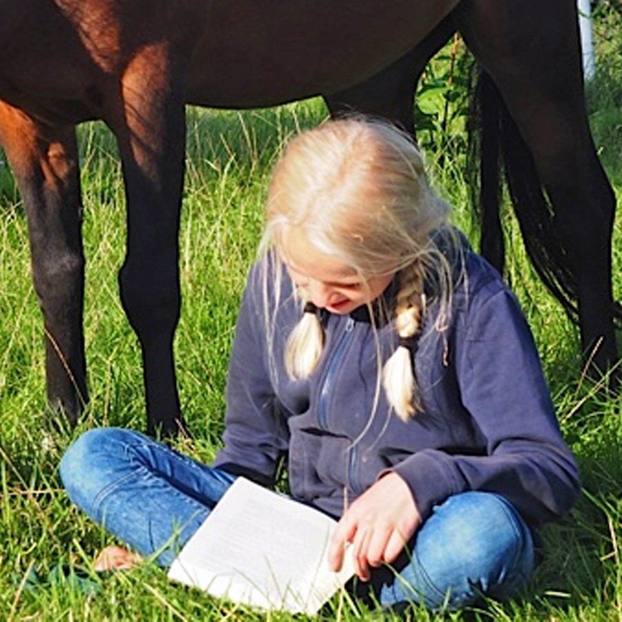 Ein Mädchen sitzt vor einem Pferd und liest ein Buch © NDR/Katharina Mahrenholtz Foto: Katharina Mahrenholtz
