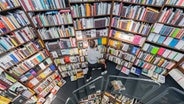 Viele Bücher in Regalen in einer Buchhandlung, eine junge Frau steht vor einem der Borde und zieht Bücher heraus © Rolf Vennenbernd/dpa +++ dpa-Bildfunk +++ Foto: Rolf Vennenbernd