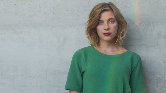 Eine junge Frau steht vor einer grauen Wand und trägt ein grünes T-Shirt. © Theresa Haugg Foto: Theresa Haugg