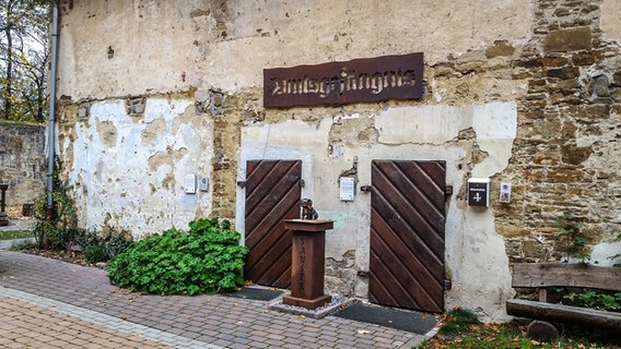 Eine Gebäudewand mit zwei Holztüren und einem Holzschild © Merle Giebeler / NDR Foto: Merle Giebeler
