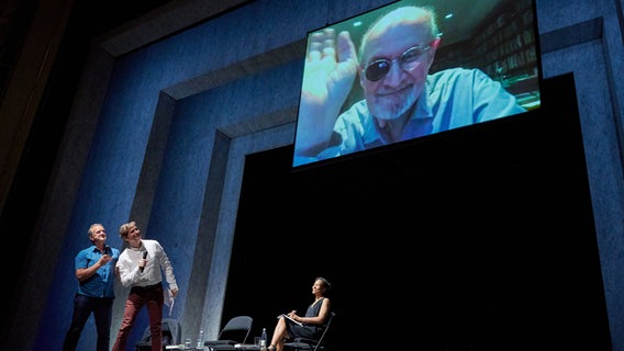 Beim Internationalen Literaturfestival Berlin stellt Schriftsteller Salman Rushdie, live aus New York zugeschaltet, sein Buch "Victory City" vor, während ihn Schriftsteller Daniel Kehlmann (2.v.l.) und Bernhard Robben (l), Übersetzer des Buches von der Bühne aus begrüßen. Schauspielerin Cynthia Micas (r) las darin. © dpa Foto: Annette Riedl