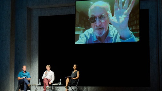 Beim Internationalen Literaturfestival Berlin stellt Schriftsteller Salman Rushdie, live aus New York zugeschaltet, sein Buch "Victory City" vor, während ihn Schriftsteller Daniel Kehlmann (2.v.l.) und Bernhard Robben (l), Übersetzer des Buches von der Bühne aus begrüßen. Schauspielerin Cynthia Micas (r) las darin. © dpa Foto: Annette Riedl