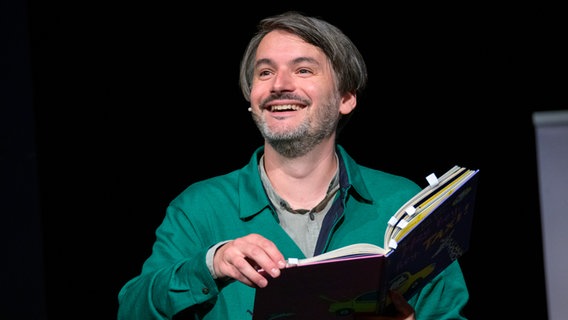 Der Schriftsteller Saša Stanišić lacht und hält ein Buch in der Hand. © picture alliance/dpa | Jonas Walzberg Foto: Jonas Walzberg
