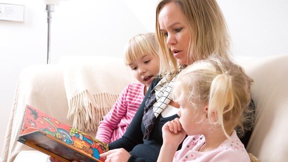 Mutter liest zwei Töchtern aus einem Kinderbuch vor. © colourbox 
