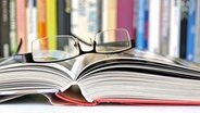 Eine Brille liegt auf einem aufgeschlagenen Buch, das vor einem Bücherregal liegt. © fotolia.com Foto: svor