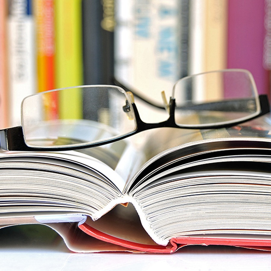 Eine Brille liegt auf einem aufgeschlagenen Buch, das vor einem Bücherregal liegt. © fotolia.com Foto: svor