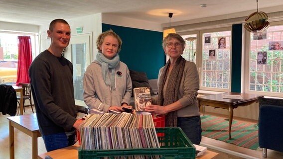 Drei Personen stehen vor einer Kiste voller Bücher und Platten und schauen freundlich nach vorne. © Antonia Reiff / NDR Foto: Antonia Reiff