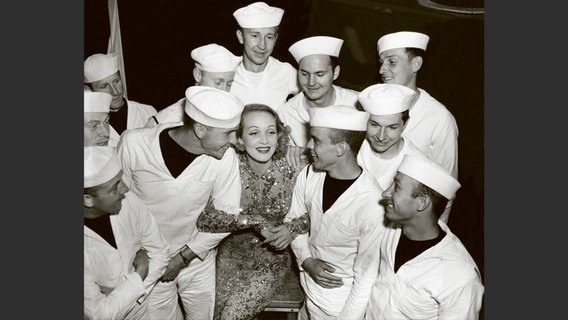 Foto aus dem Bildband "Marlene Dietrich an der Front": Schwarzweiß-Foto von einer blonden Frau, umringt von Marinesoldaten © Deutsche Kinemathek - Marlene Dietrich Collection Berlin 