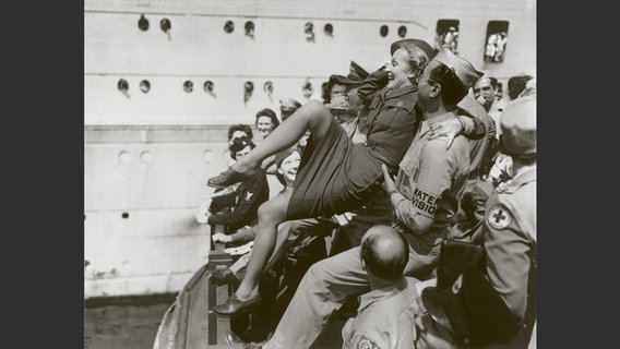 Foto aus dem Bildband "Marlene Dietrich an der Front": Schwarzweiß-Foto von einem Marine-Soldaten, der eine blonde Frau in die Luft hebt. © Deutsche Kinemathek - Marlene Dietrich Collection Berlin 