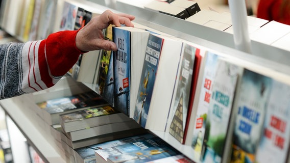 Eine Hand greift nach Büchern in einem Regal. © picture alliance / Jens Kalaene/dpa-Zentralbild/dpa | Jens Kalaene 