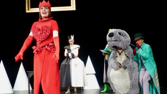 Auf der Bühne stehen vier Personen. Eine Frau im Vordergrund trägt ein rotes Kostüm, dahinter steht eine Frau mit einem schwarz, weißen Kostüm. © Krüger Foto: Krüger