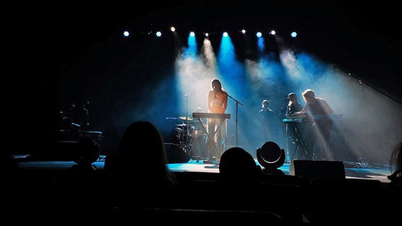 Auf einer Bühne, die in blaues Licht getaucht ist, spielen Musiker. © NDR Foto: Nora Reinhardt