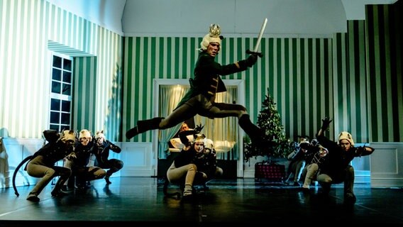 Mehrere Menschen in Kostümen sind auf einer Bühne, im Vordergrund springt jemand. © Peter van Heesen Foto: Peter van Heesen