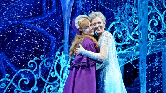 Die Darstellerinnen Sabrina Weckerlin (Eiskönigin Elsa, r.) und Celena Pieper (ihre Schwester Anna) umarmen sich bei einer Probe für das Musical "Die Eiskönigin" auf der Bühne im Stage Theater an der Elbe. © NDR Foto: Patricia Batlle