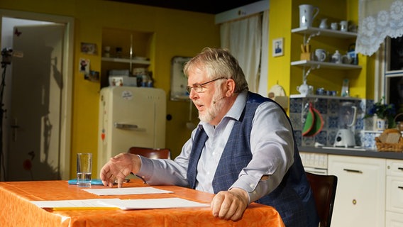 Ein Mann in Oberhemd und Weste mit grauen Haaren und Bart sitzt an einem Küchentisch und liest von einem Blatt ab. Ein Mann in Oberhemd und Weste mit grauen Haaren und Bart sitzt an einem Küchentisch und liest von einem Blatt ab. © NDR Foto: Lornz Lorenzen