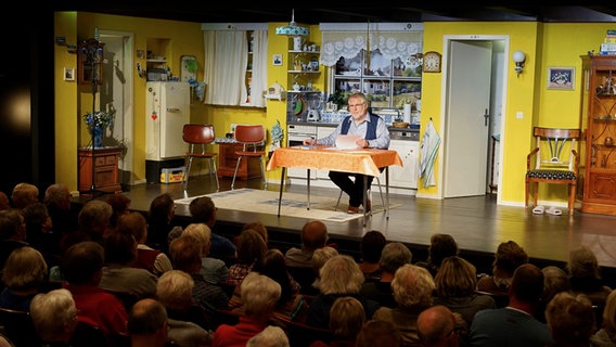 Ein Mann in Oberhemd und Weste mit grauen Haaren und Bart sitzt an einem Küchentisch und liest von einem Blatt ab. Ein Mann in Oberhemd und Weste mit grauen Haaren und Bart sitzt an einem Küchentisch und liest von einem Blatt ab. © NDR Foto: Lornz Lorenzen