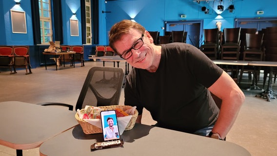 Jan-Peter Petersen sitzt am Tisch. Darauf steht ein Handy, auf dem sein Sohn Max Beier zu sehen ist. © NDR Foto: Peter Helling