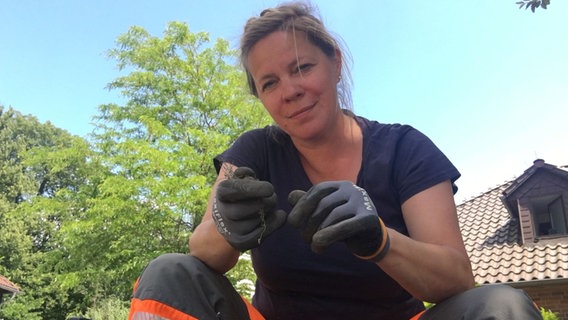 Eine Frau sitzt mit einem dunkelblauen T-Shirt und einer orangenen Arbeitshose auf dem Boden. © Juschka Spitzer Foto: Juschka Spitzer