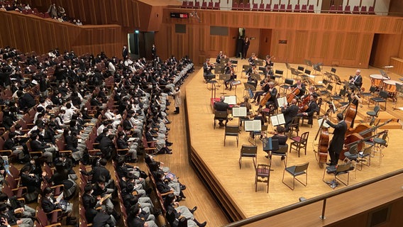 Ein Orchester sitzt auf einer Bühne, vor ihnen sitzt das Publikum. © Friederike Westerhaus / NDR Foto: Friederike Westerhaus