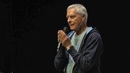 John Neumeier hält vor schwarzem Hintergrund sichtlich berührt das Mikro zwischen den Händen © NDR Screenshot 