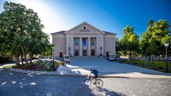 Ein Radfahrer fährt bei Sonnenschein am Landestheater Neustrelitz vorbei. © picture alliance/dpa/dpa-Zentralbild Foto: Jens Büttner