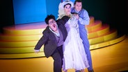 Eine als Braut in Weiß gekleidete Frau wird von zwei Männern umrahmt, die alle drei erschrocken nach vorn blicken. © Theater Basel Foto: Thomas Aurin