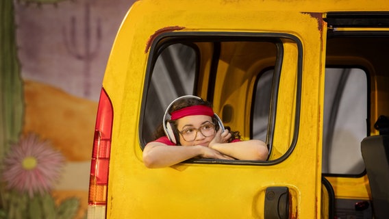 Ein Mädchen mit Kopfhörern schaut aus dem Fenster eines gelben Autos © Silke Winkler Foto: Silke Winkler