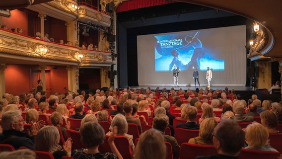 Ein großer Theatersaal voller Menschen mit Blick auf die Bühne, auf der drei Menschen stehen. Im Hintergrund auf der Leinwand steht: 16. Internationale Tanztage, 9. - 18. Mai. © Stephan Walzl 