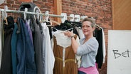 Die Kostümschneiderin Regine Meinardus hängt ein Kleid an eine Kleiderstange. © NDR Foto: Helgard Füchsel