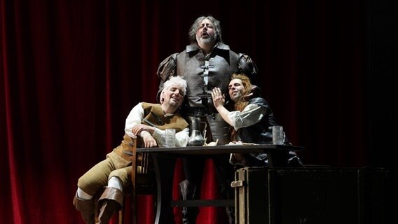 Stefano Meo als Falstaff steht wie ein Fels in der Brandung in der Mitte - links und rechts neben ihm: Matteo Maria Ferretti als Pistola und Konrad Furian als Bardolfo bei der Aufführung von Verdis "Falstaff". © Oper Kiel Foto: Olaf Struck