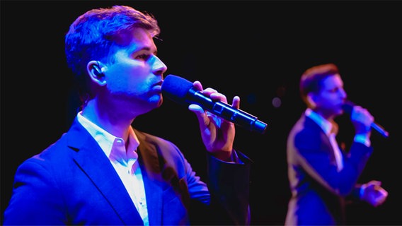 Zwei junge Männer im Anzug stehen auf der Bühne und singen ins Mikrofon © The Real Group 