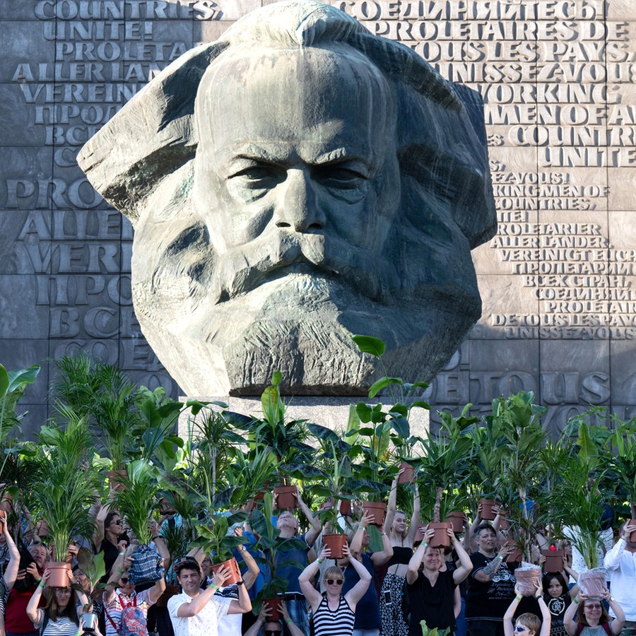 Menschen tragen jeweils eine Zimmerpflanze durch die Straßen von Chemnitz - vor dem Karl-Marx-Monument, dem Wahrzeichen der Stadt © Hendrik Schmidt/dpa +++ dpa-Bildfunk Foto: Hendrik Schmidt