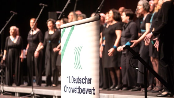Sängerinnen und Sänger hinter dem Plakat zum "Deutschen Chorwettbewerb 2023" (Senior Jazzchor) in Hannover © Helge Krückeberg Foto: Helge Krückeberg