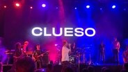 Eine Band spielt auf einer Theaterbühne, im Hintergrund wird der Künstlername "Clueso" projiziert. © NDR Foto: Sabine Hausherr