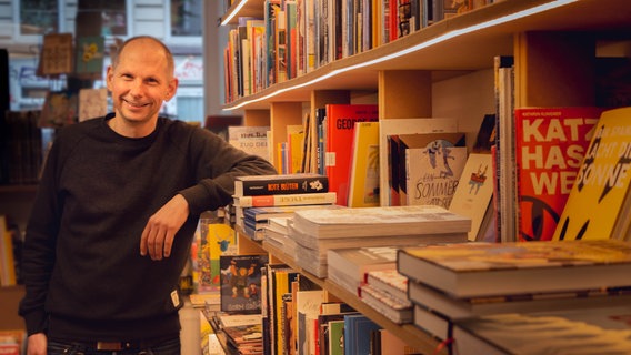 Hans Ebert steht neben einem Bücherregal voller Graphic Novels © NDR.de Foto: Christina Grob