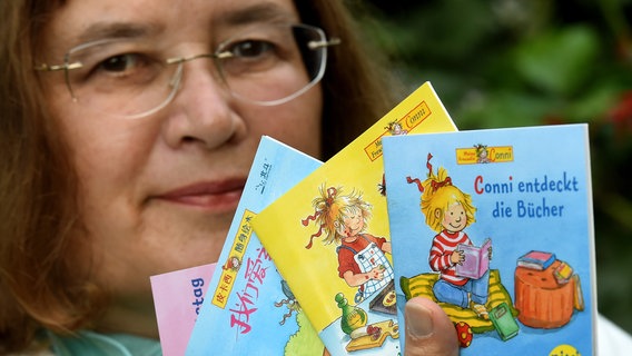 Eine Frau mit Brille und braunem Haar hält vier Pixi-Bücher in die Kamera. © picture alliance / dpa | Holger Hollemann 