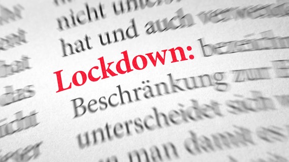 Ein aufgeschlagenes Wörterbuch, in dem der Begriff "Lockdown" rot markiert ist. © picture alliance / Shotshop | Zerbor 