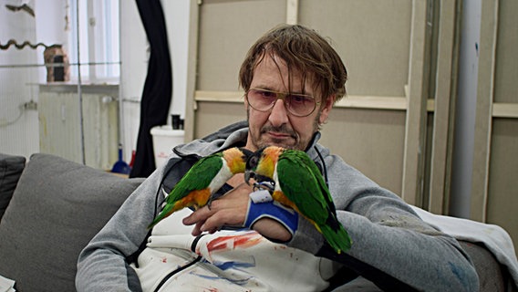 Daniel Richter hält zwei Papageien in den Händen. © B / 14 Film Foto: Marvin Hesse
