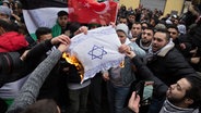 Teilnehmer einer Demonstration verbrennen eine selbstgemalte Fahne mit einem Davidstern © picture alliance/dpa/Jüdisches Forum für Demokratie und gegen Antisemitismus e.V. 