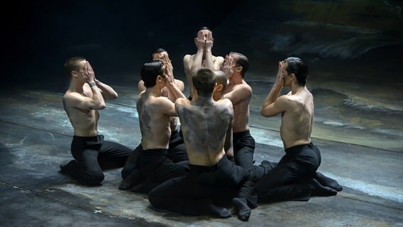 Mehrere Tänzer knien mit nacktem Oberkörper dich beieinander auf der Bühne. © Staatsoper Hannover Foto: Ralf Mohr