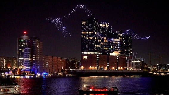 Beleuchtete Drohnen des Künstlerduos Drift fliegen in Formation "Breaking Waves" über der Elbe vor der Elbphilharmonie im Rahmen der Eröffnung des Musikfests Hamburg. © Georg Wendt/dpa +++ dpa-Bildfunk +++ Foto: Georg Wendt