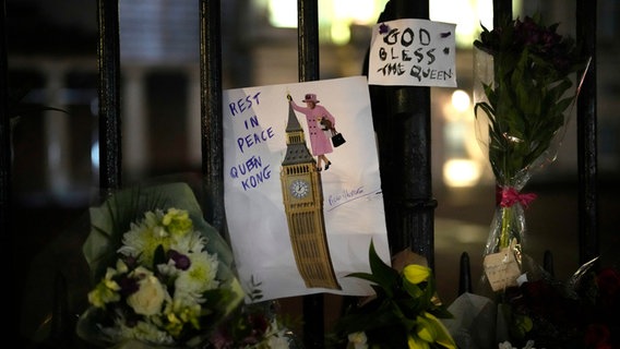 Vor dem Zaun am Buckingham Palace liegen Blumen und ein gemaltes Bild © picture alliance/dpa/AP Foto: Christophe Ena